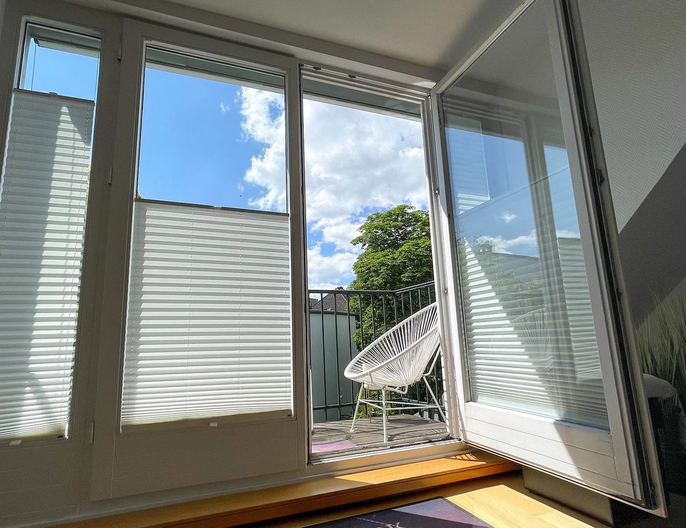 Geöffnete hohe Altbaufenster mit Blick auf den Balkon und den blauen Himmel